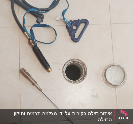 כלי עבודה וצינור ליד פתח ביוב פתוח